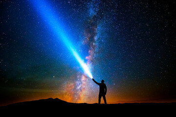 Man with flashlight pointed at the starry sky - obrazy, fototapety, plakaty
