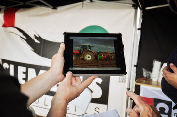 Fototapeta Osoba pokazująca na tablecie prezentację pracy ciągnika z pługiem. Prezentacja na targach ogrodniczych obraz