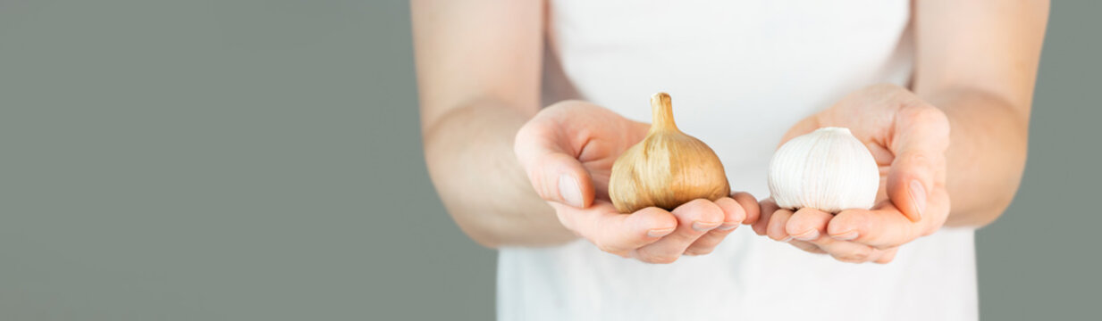 A man in a white t-shirt on a green background holds garlic and black garlic bulbs in his hands. fermented garlic in man's hands. Fermented food, healthy nutrition, self-care. Copy space. Banner