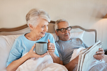 We still like the good old fashioned newspaper. Cropped shot of a senior man reading a newspaper in bed while his wife drinks a cup of coffee. - Powered by Adobe