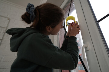 Young woman sealing the window glass using adhesive tape