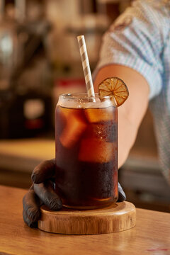 hombre sirviendo vaso de bebida oscura sobre una mesa y un popote de cart&oacute;n