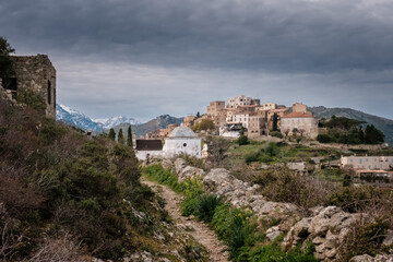 Fototapeta na wymiar Track leading towards the hilltop village of Sant'Antonino in the Balagne region of Corsica with snow capped mountains in the distance