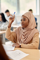 Black student in hijab raises her arm to ask question during lecture in classroom.