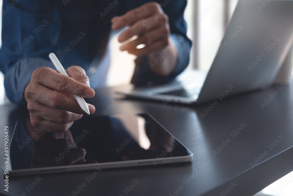 Poster close up of business man using digital tablet and working on laptop computer on office table