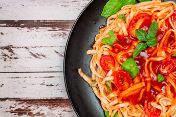 Spaghetti pasta with an exquisite homemade tomato sauce with homemade basil leaves served on a black plate on a rustic table. Copy space. Close up. Top view.