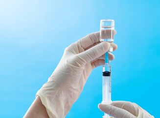 Doctor's hand holding syringe and ampule on blue background