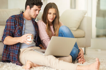 We do all our shopping online. Shot of a happy young couple using a laptop together while relaxing in their lounge at home.