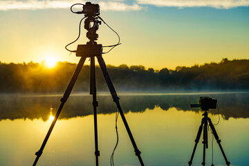 Camera on tripod take photo from sunrise over lake