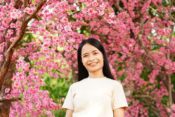 Asian woman smiling happily in a tourist place beautiful blooming pink flower background