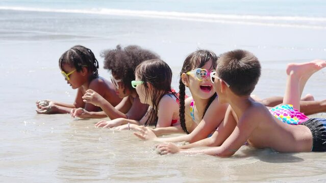 Group of Diversity little child boy and girl friends lying on tropical beach and playing in sea water together on summer vacation. Happy children kid enjoy and fun outdoor lifestyle on beach holiday