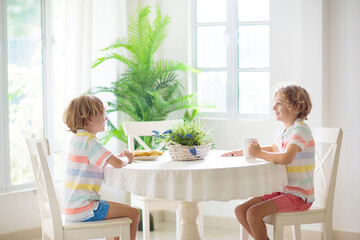 Naklejka premium Kids eating breakfast in white kitchen.