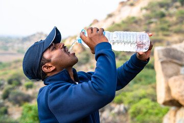 Thirsty hiker drinking water while on top of hill during summer - concept of relaxation heat wave...
