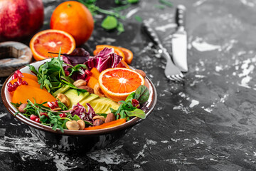 Fototapeta na wymiar Healthy vegetarian buddha bowl salad with avocado, persimmon, blood orange, nuts, spinach, arugula and pomegranate on a dark background, Long banner format, top view