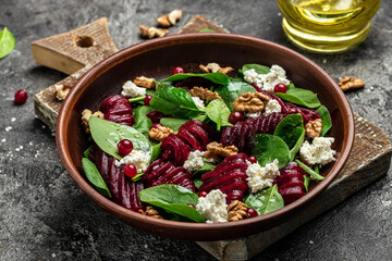 Beet or beetroot salad with baby spinach, cheese, nuts, cranberries on plate with fork, dressing and spices on dark background, Food recipe background. Close up