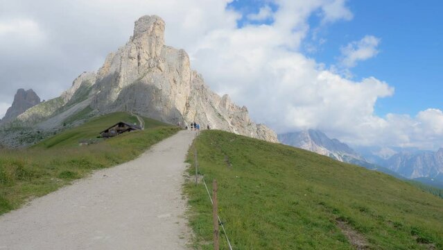 Pathway in high mountain in the foreground cuts a green meadow in two and in the background reaches a rock peak of the Dolomites that stands out against a blue sky