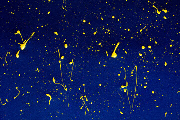 Naklejka premium closeup of yellow paint drops on blue paper background