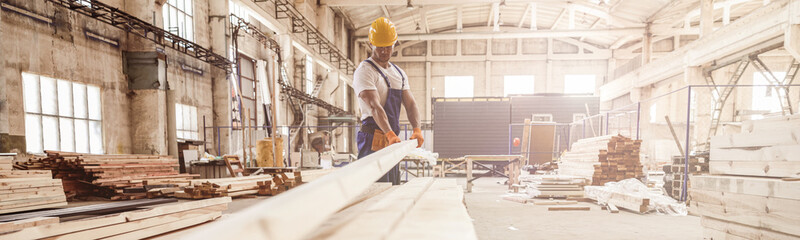 Male worker carrying wooden plank at construction site