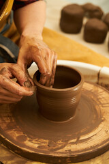 Fototapeta na wymiar A Potter works with red clay on a Potter's wheel in the workshop..Women's hands create a pot. Girl sculpts in clay pot closeup. Modeling clay close-up. Warm photo atmosphere.