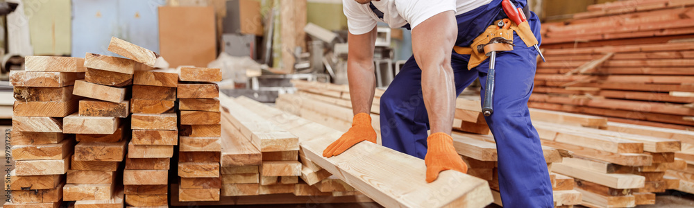 Wall mural handsome male builder holding wooden plank at construction site