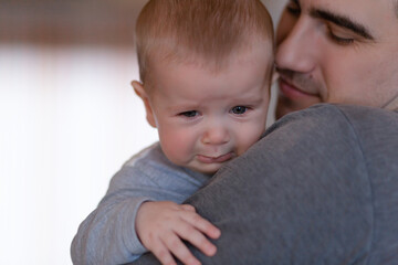 Closeup Sad young blond boy crying on father hands in room. Man holds son, hugs and comforts. Family love, care and moral support, baby's tears, daddy's arms. Dad consoling crying child