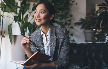 Carefree female with eyeglasses and education textbook for studying and learning smiling while...