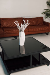 On a black glass table is a white vase of flowers in the office