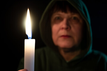 An elderly woman in the dark holds a candle in her hands.