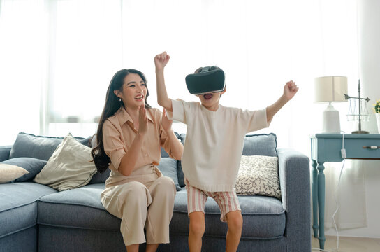 Smiling mother looking son playing games using virtual reality headset(VR) at home. Technology future concept.