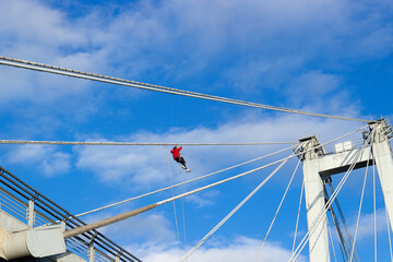 Unrecognizable industrial climber working on a cable on a cable-stayed bridge against cloudy sky...