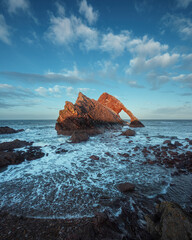 Landscape of natural sea arch lit by the setting sun. Famous rock formation on the Moray Coast,...