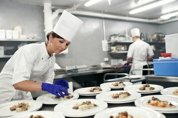 Making dinner into a masterpiece. Shot of a chef plating food for a meal service in a professional kitchen.