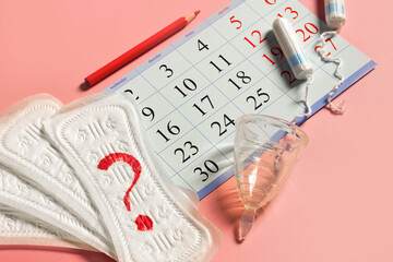 Woman menstrual cup, tampons, calendar, control of the regular cycle, pencil and sanitary pad napkin with a question close up