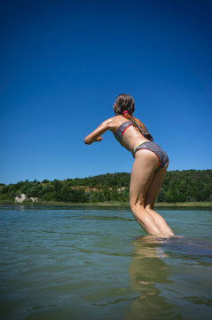 A little cute girl in a swimsuit jumps into the blue water of a career lake.