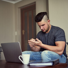 Memo remember to buy a notebook. Shot of a serious young man making notes on his hand while he works on his laptop at home.