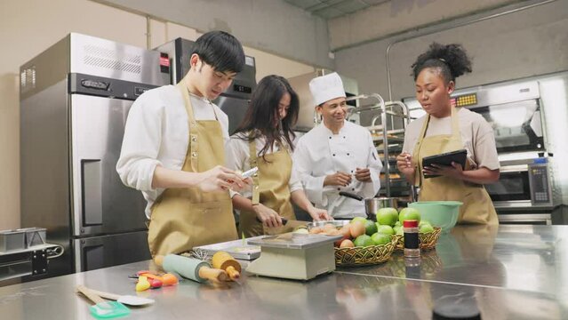 Cooking  course , senior Asian male chef in cook uniform teaches young asian and african american people cooking class students to prepare, mix ingredients for pastry foods, in restaurant stainless 
