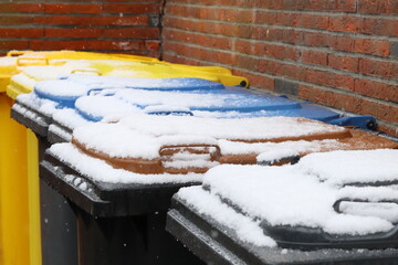 Rubbish cans with colorful hoods covered with snow. Waste separation. Recycling in Germany. Selected focus.