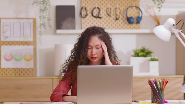 Asian woman sitting at desk in front of laptop stressed out face and headache shows her stressful  with work from home office. Female thinking about work mistake or workload has depression.