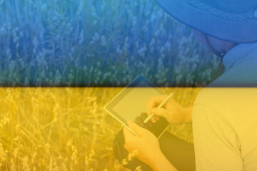 Ukraine. Digital farm. Portrait of farmer seating in gold wheat field and writing on tablet. Young man wearing cowboy hat in field examining wheat crop. Oats grain industry. Modern produce Oats plant