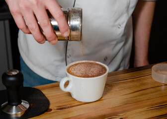 Fototapeta na wymiar barista sprinkling chocolate on coffee in cafe