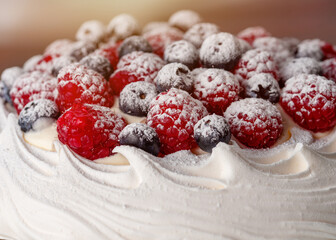 meringue cake with blueberries and raspberries on a plate on green background