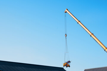 Mobile crane lifting telehandler above the building to place it in the working area without an...