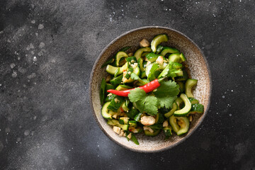 Asian Broken Spicy Cucumbers salad with coriander, ginger, pepper chili, black vinegar on dark black background. Popular Chinese appetizer. Top view.