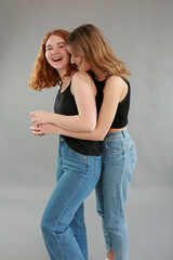 two beautiful young girls model blonde and redhead hugging. model in jeans and black tops on a gray background. girlfriends hugging. female friendship. studio shooting