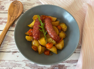 Salsiccia al forno. Italian frying sausage or bratwurst with potatoes, cherry tomatoes, red onions...