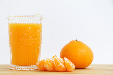 Close up of a glass of natural Mandarin orange juice with four peeled orange pieces and a full orange on a wooden board, full of vitamin c and nutritional goodness, healthy lifestyle