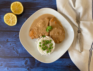 Austrian chicken schnitzel naturally fried with sauce, rice and peas.