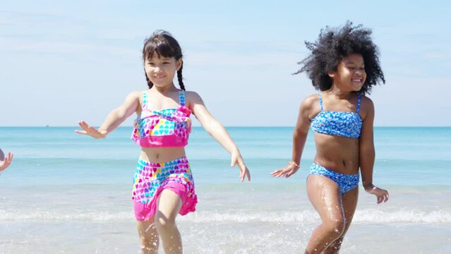 Group of Diversity little child boy and girl friends running and playing in sea water on tropical beach together on summer vacation. Happy children kid enjoy and fun outdoor lifestyle on beach holiday