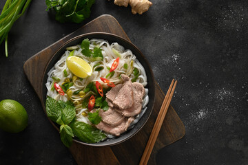 Pho Bo soup with beef, rice noodles, lime, chili pepper in bowl on black background. Vietnamese and Asian cuisine.