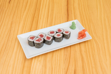 Portion of maki stuffed with white rice with vinegar and almadraba red tuna with nori seaweed with wasabi and ginger on a pine wood table